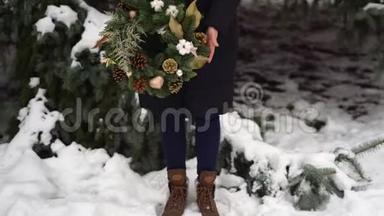 穿着靴子的女孩的腿，手里<strong>拿着</strong>圣诞<strong>花环</strong>。 冬天下雪